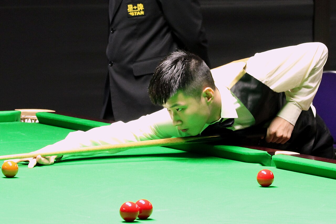 Young Asian snooker player prepares to take a shot at the snooker table