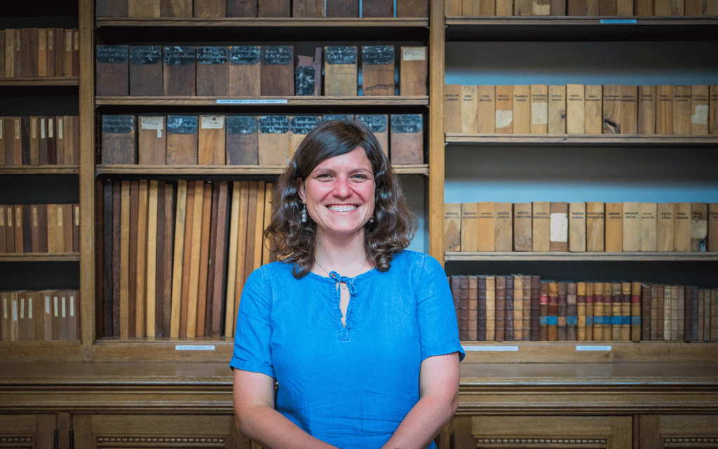Woman in blue dress smiling at camera, with bookshelves in background