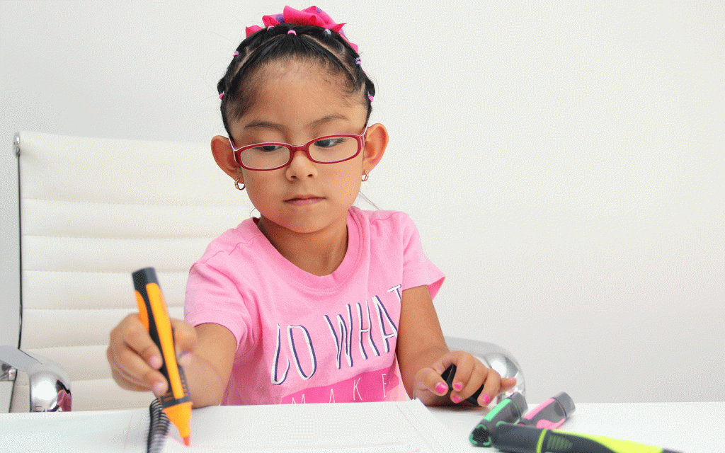 Young girl writing in a notebook with marker pens